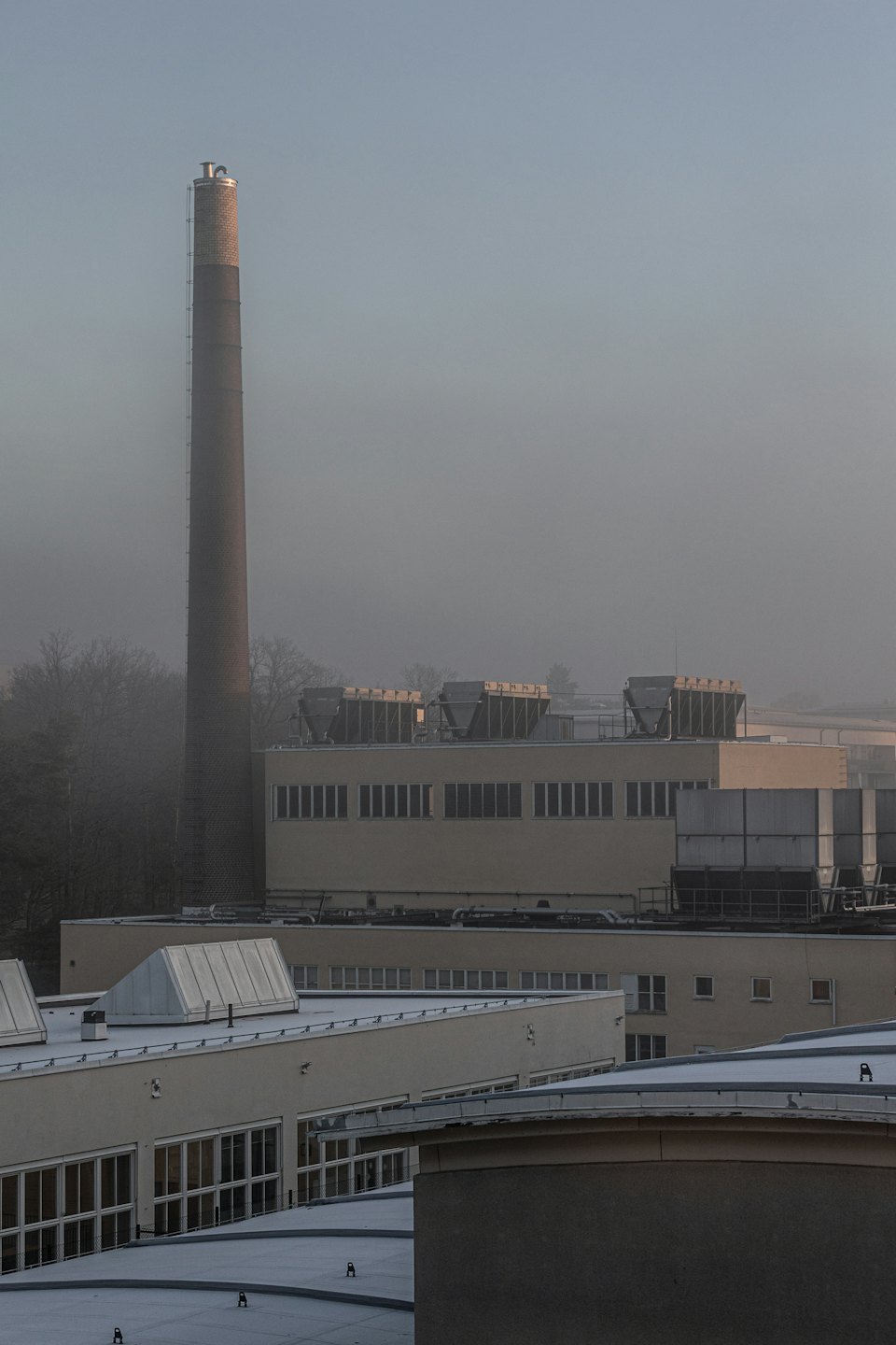 Complejo industrial con una alta chimenea de ladrillo parcialmente oculta por la niebla.