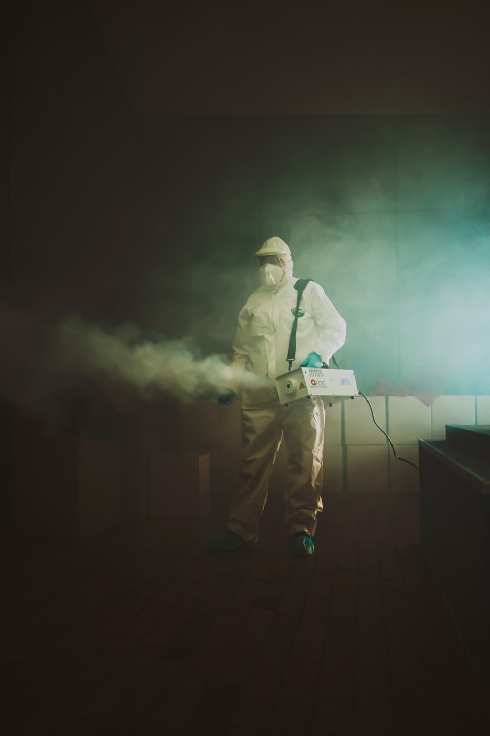 Trabajador de saneamiento con traje de materiales peligrosos usa máquina de nebulización.